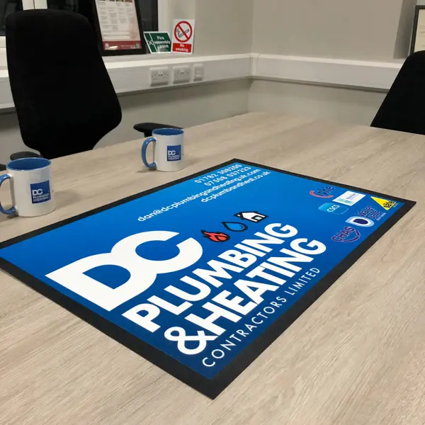 DC Plumbing & Heating branded floor mat and mugs on an office table
