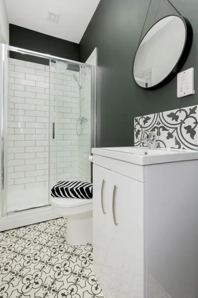 Shower room with round mirror, vanity unit and patterned floor tiles